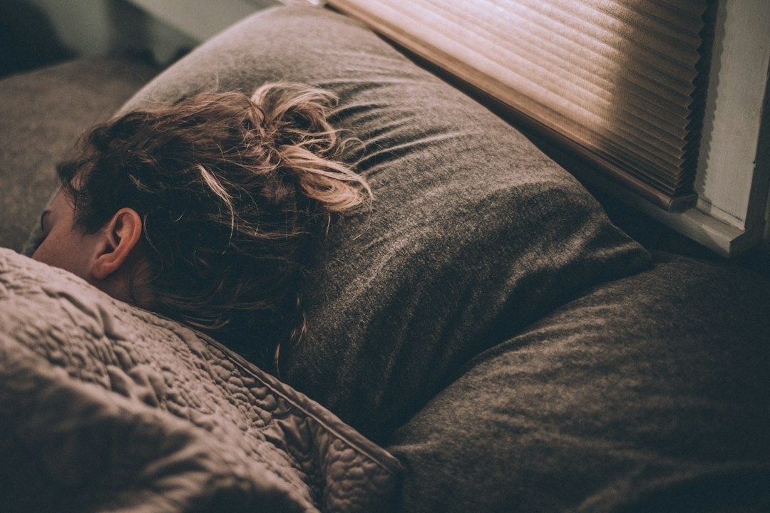 Person som sover under ett täcke i ett mörkt sovrum